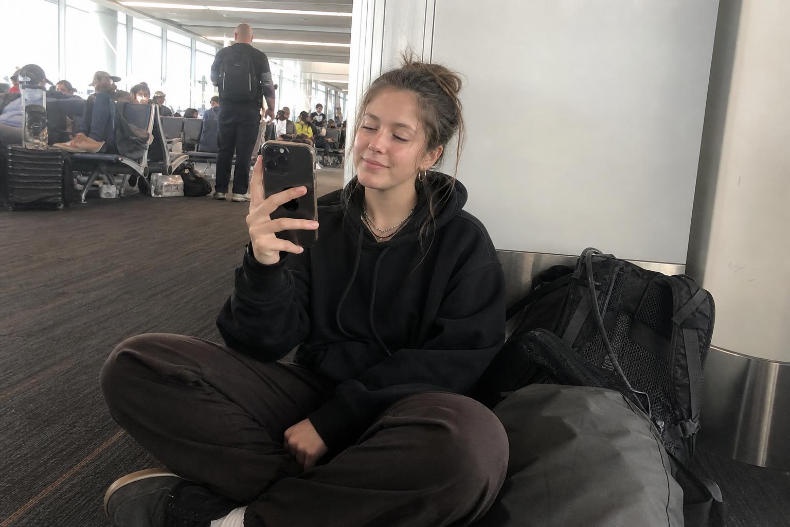 Young backpacker on a mobile video chat while waiting at a busy airport gate during travel